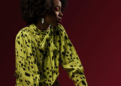 Model wears yellow polka dot top and looks to side on red background.